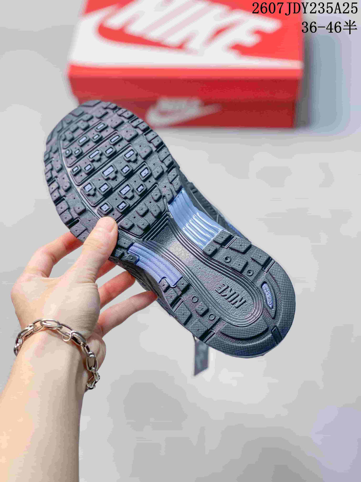 Underside of a blue and dark gray Nike P-6000 sneaker showing the textured rubber outsole and lugged tread; source overlay shows style code 2607JDY235A25 and size range 36–46.5.