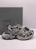 Side view of brown, gray, cream, and black Balenciaga 3XL sneakers with a branded box in the background.