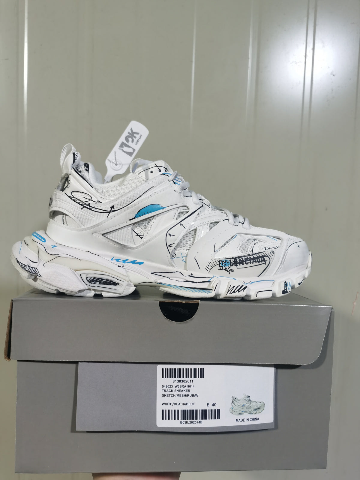 Side profile of the white, black, and blue sneaker displayed on its box; the box label shows style code 9014 and sample size EU 40.