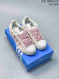 Pair of white and pink adidas Superstar sneakers displayed on a blue shoebox, with the shell toes and ruffled pink laces visible.