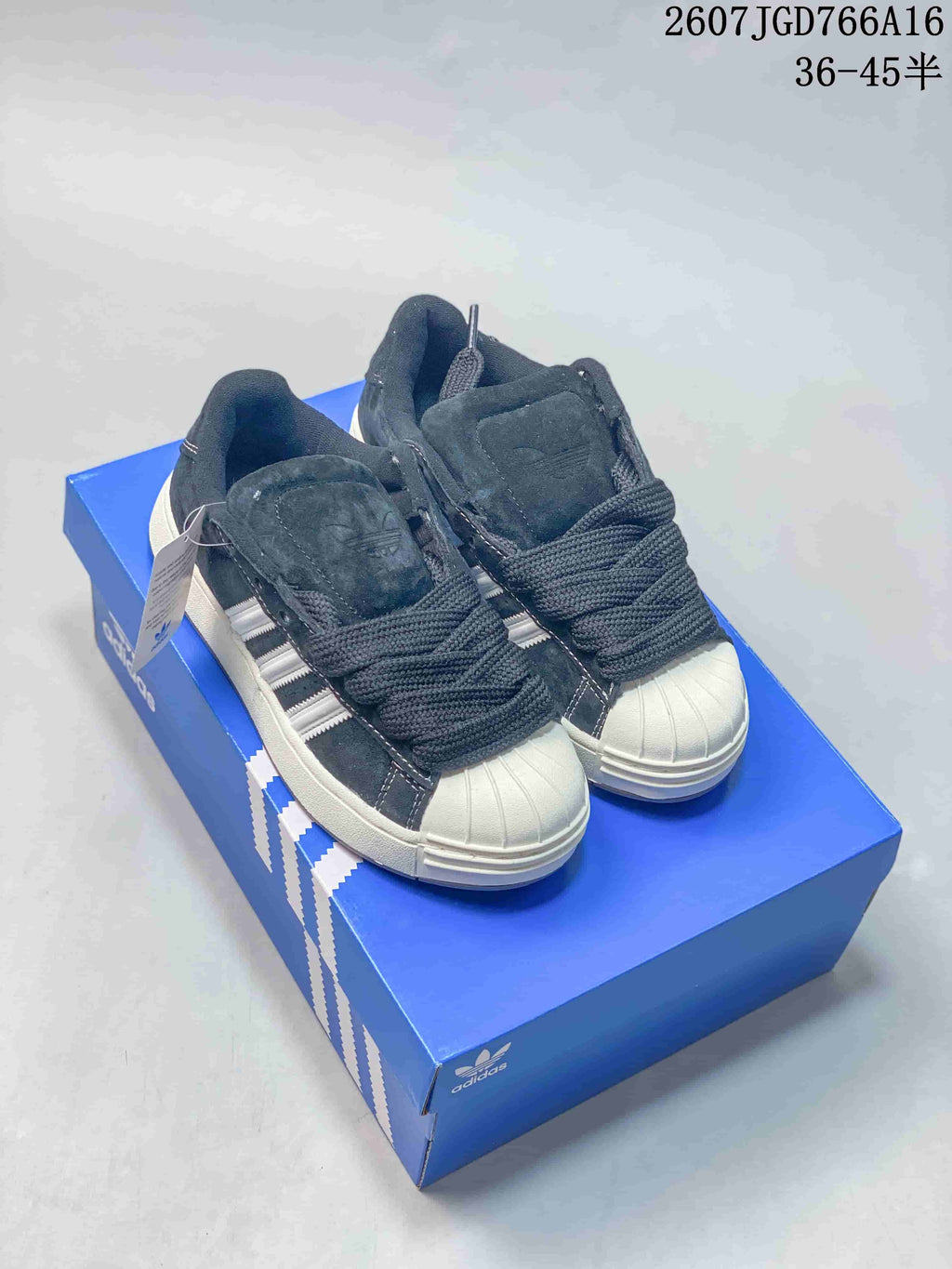 Pair of black and gray shell-toe adidas sneakers displayed on a blue adidas shoebox, with the style code and size range visible at the top.