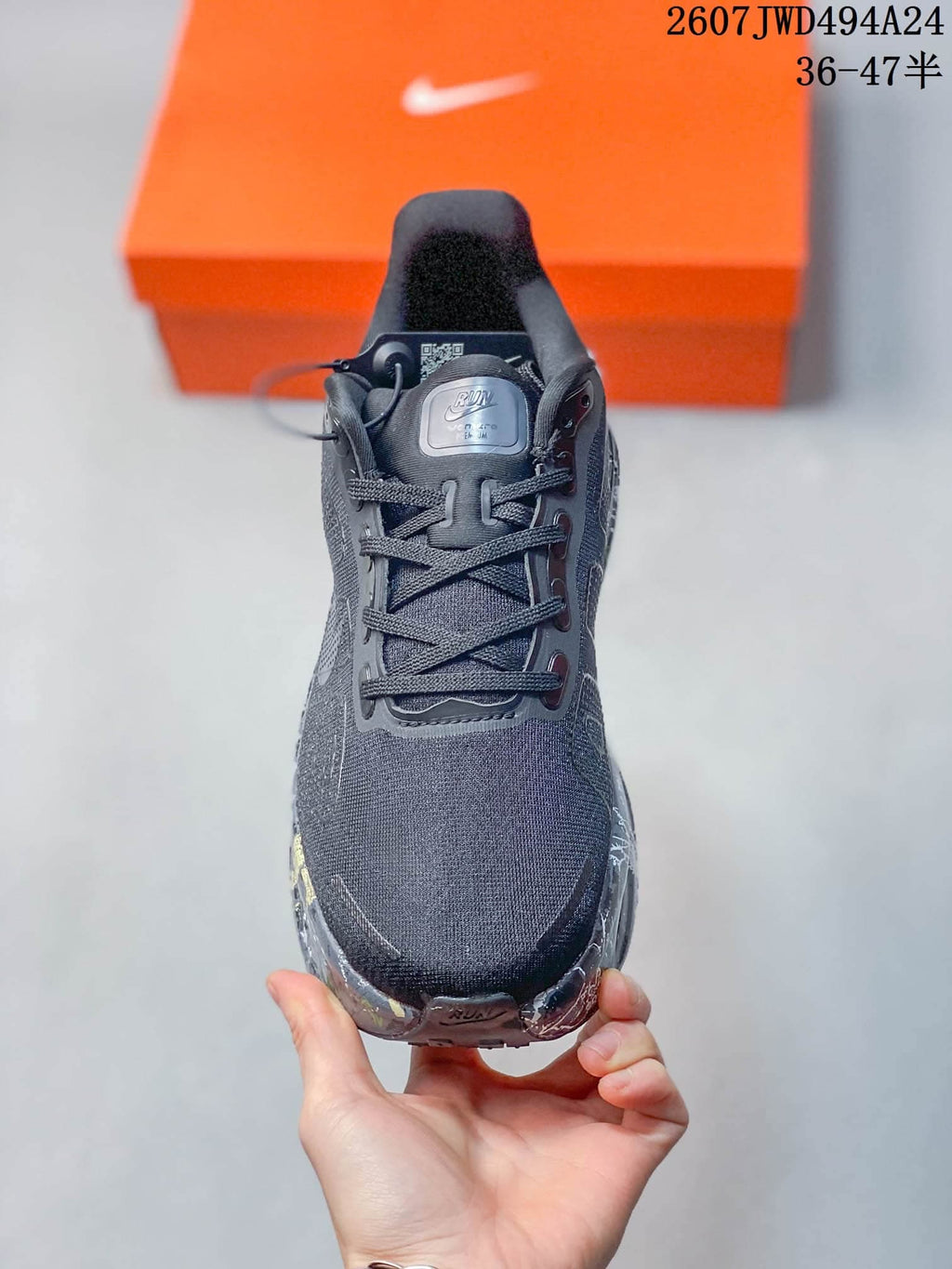 Front view of the sneaker showing the dark mesh-style upper, tongue branding, and lace closure.
