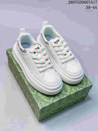Pair of white Gucci sneakers photographed from above on a green patterned box, showing the lace-up fronts and colorful collar accents.