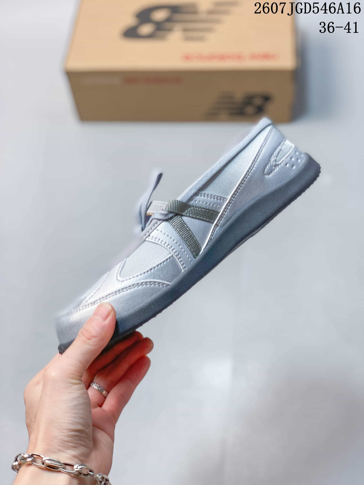 Side view of the silver-gray New Balance shoe showing the rounded profile, cross straps, stitched panels, and dark outsole.