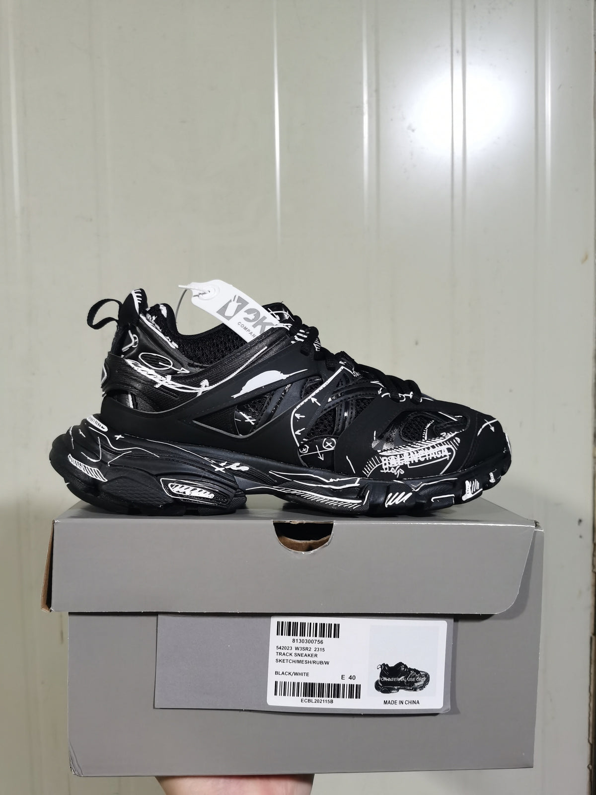 Black and white track sneaker displayed on its box, showing the layered upper, graphic detailing, chunky sole, and box label.