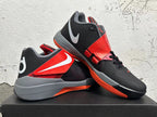 Pair of black and red basketball shoes displayed at an angle, showing the strap and side branding