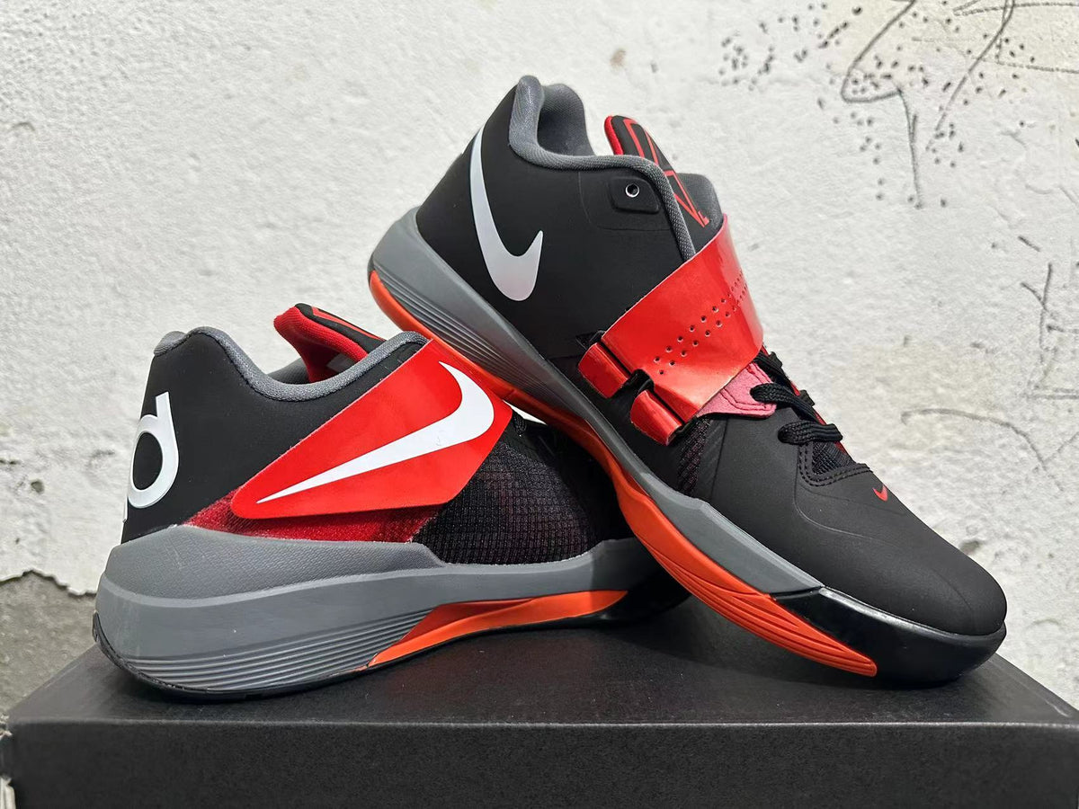 Pair of black and red basketball shoes displayed at an angle, showing the strap and side branding