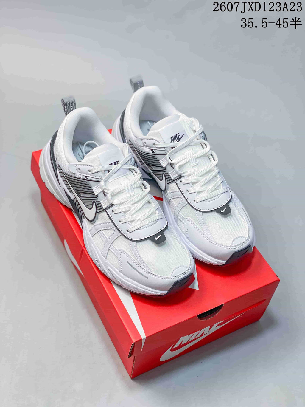 Pair of white and black Nike V2K Run sneakers displayed on a red shoebox.