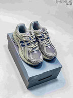 Pair of grey and silver New Balance M1906AD sneakers with navy accents on a shoebox