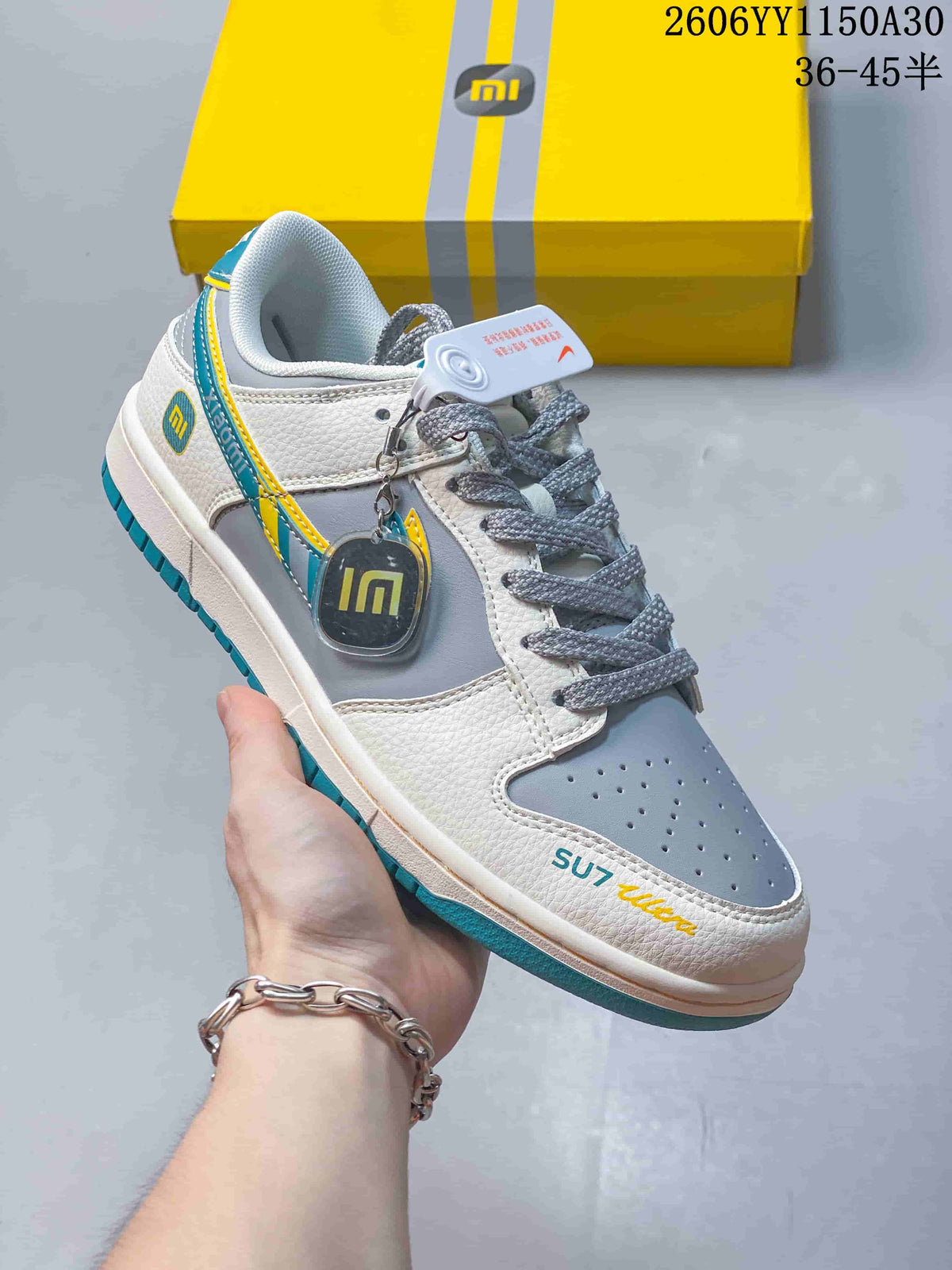 Angled view of a white and gray low-top sneaker with turquoise and yellow details and “SU7 Ultra” text.