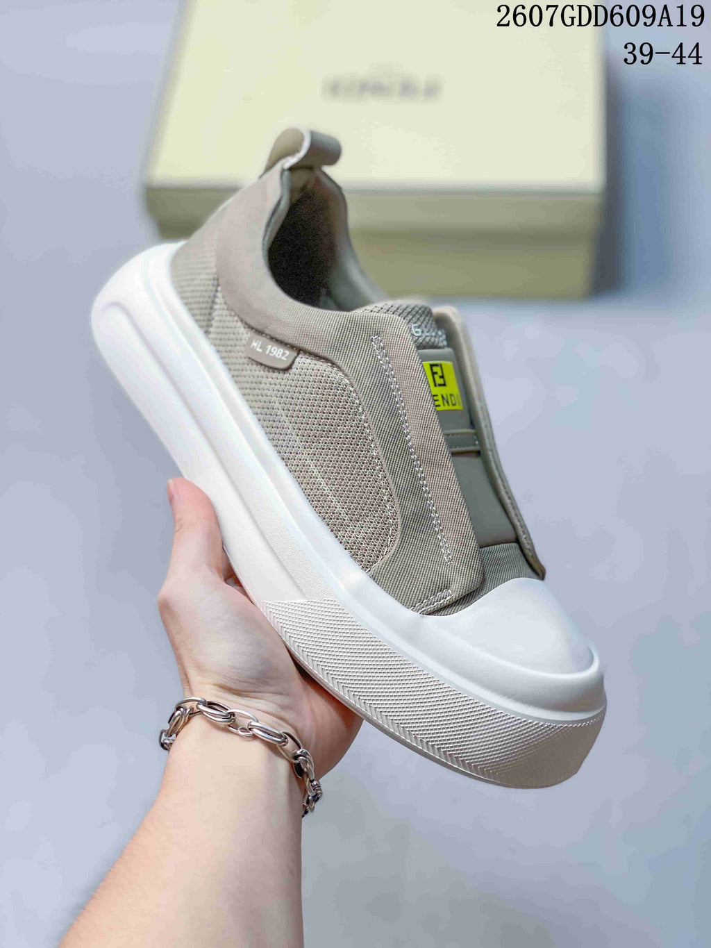 Side view of a taupe Fendi slip-on sneaker showing the elasticated upper, heel pull tab, side detail, and white textured sole; image text lists sizes 39–44.