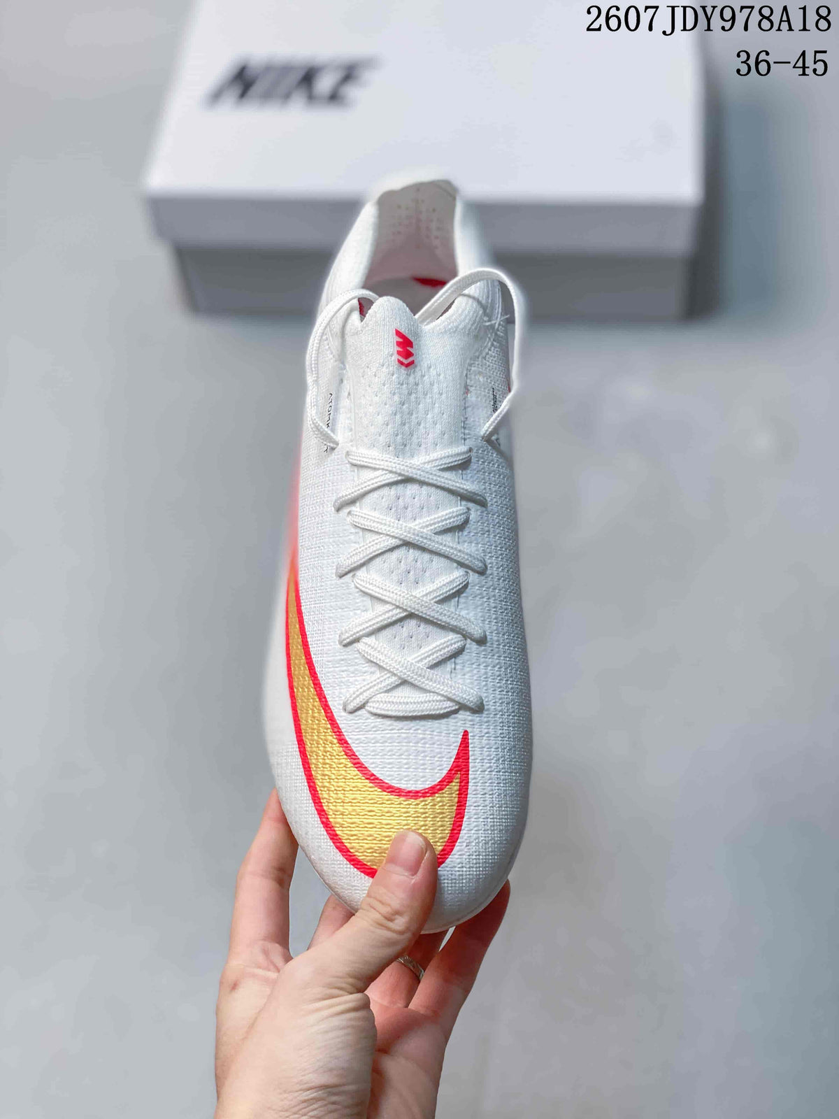 Top view of the white soccer cleat showing the lace-up closure and large gold Swoosh outlined in red.