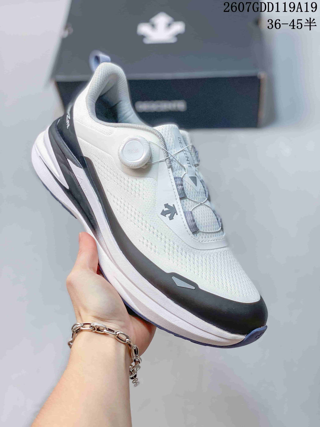 Angled side view of the white DESCENTE running shoe showing the BOA-style dial, dark toe overlay, and layered sole.