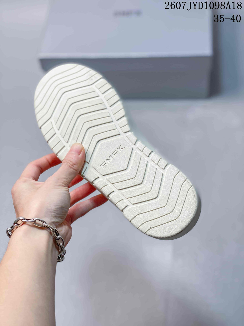 Close view of the white sneaker outsole with a geometric grooved tread pattern and central embossed lettering.