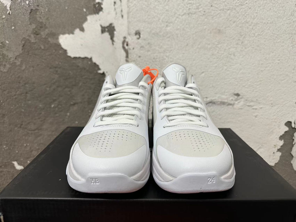 Front view of silver and white basketball shoes showing laces, perforated toe panels, and Kobe tongue emblems.