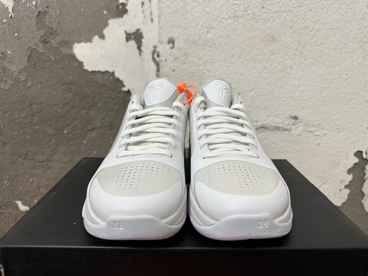 Front view of silver and white basketball shoes showing laces, perforated toe panels, and Kobe tongue emblems.