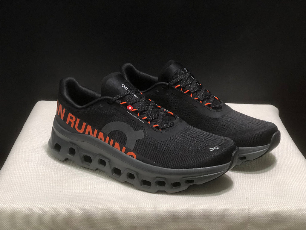 Three-quarter view of the pair showing the black upper, orange details, and raised dark outsole.