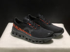 Three-quarter view of the pair showing the black upper, orange details, and raised dark outsole.