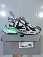 Puma 9012 sneaker displayed on its box, showing a green illuminated heel accent and the grey, white, and black colorway.