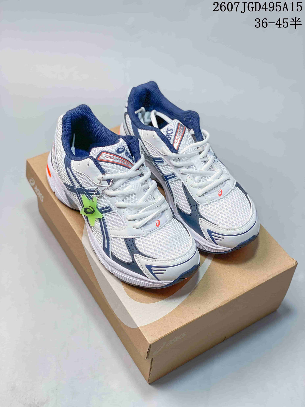 Pair of white ASICS GEL-1130 sneakers with navy and orange details displayed on a shoebox; image text shows style code 2607JGD495A15 and size range 36-45.5.