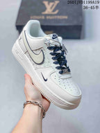 White Nike low-top sneaker held by hand, showing patterned side panels, dark Swoosh trim, Air midsole branding, and dark laces.