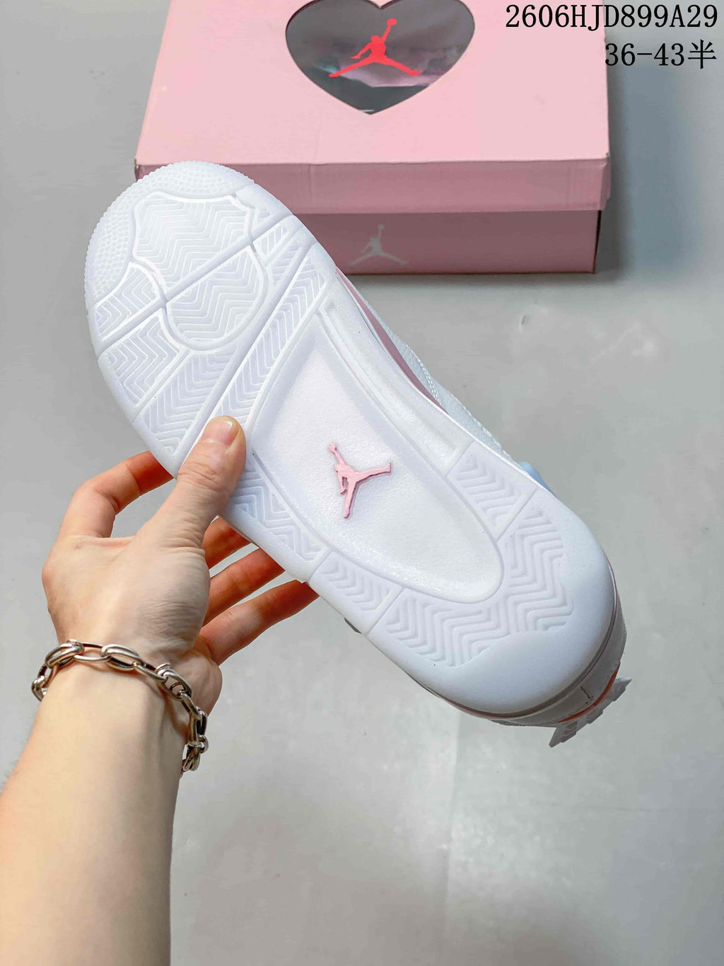 Outsole view of a white Air Jordan 4 Retro sneaker with a pink Jumpman emblem