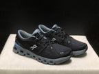 Three-quarter view of the black lace-up shoes with gray soles and blue heel accents.