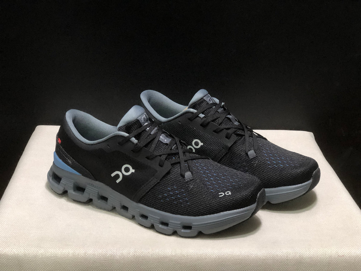 Three-quarter view of the black lace-up shoes with gray soles and blue heel accents.