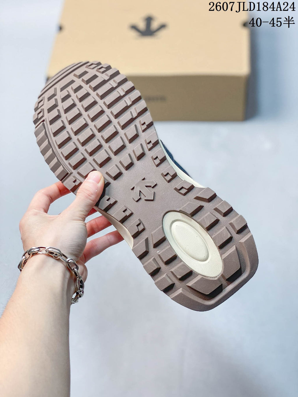 Close view of the sneaker outsole showing a block-pattern tread and central DESCENTE-style emblem.