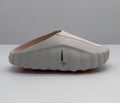Side view of a light pink and white Nike slide sandal with a perforated upper strap and orange outsole details.