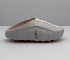 Side view of a light pink and white Nike slide sandal with a perforated upper strap and orange outsole details.