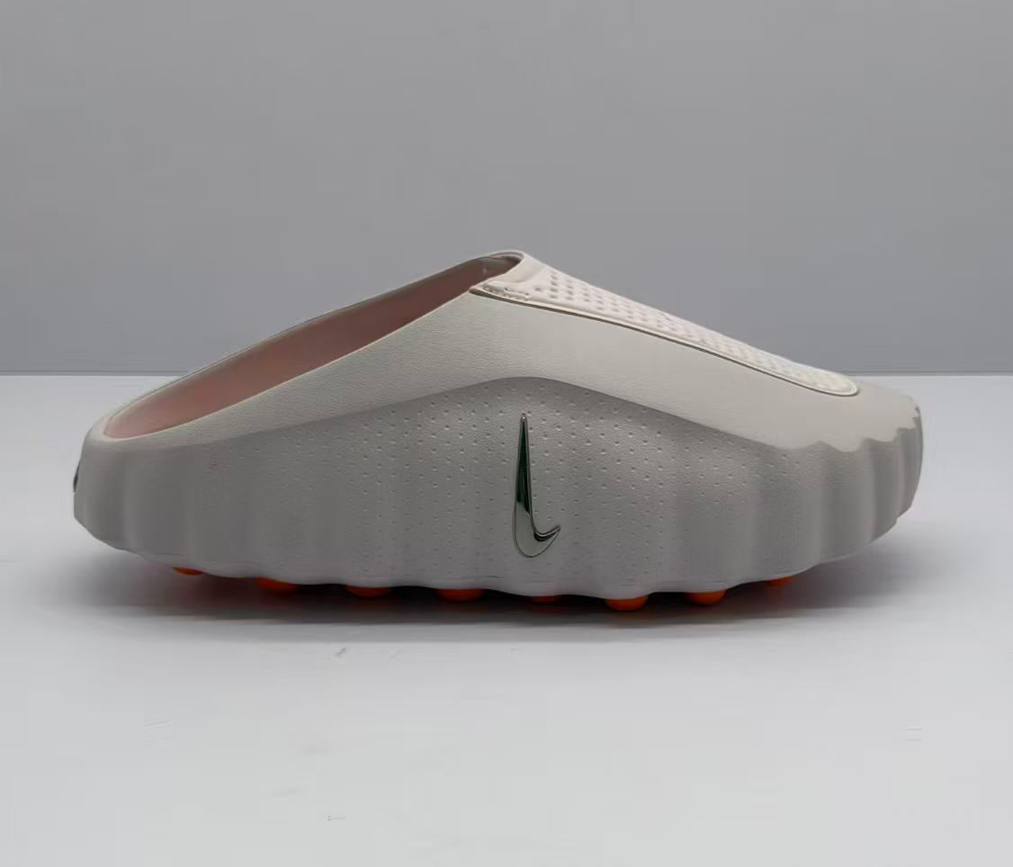 Side view of a light pink and white Nike slide sandal with a perforated upper strap and orange outsole details.