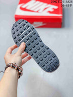 Close view of the black textured outsole with raised rectangular tread blocks, held in front of a red shoebox.