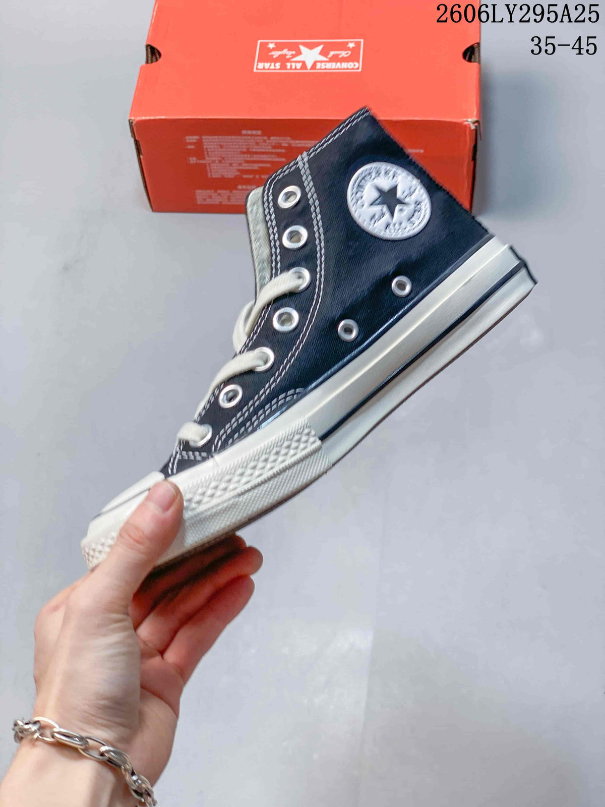 Side view of a navy Converse high-top sneaker with white laces, silver eyelets, contrast stitching and a white rubber sole.